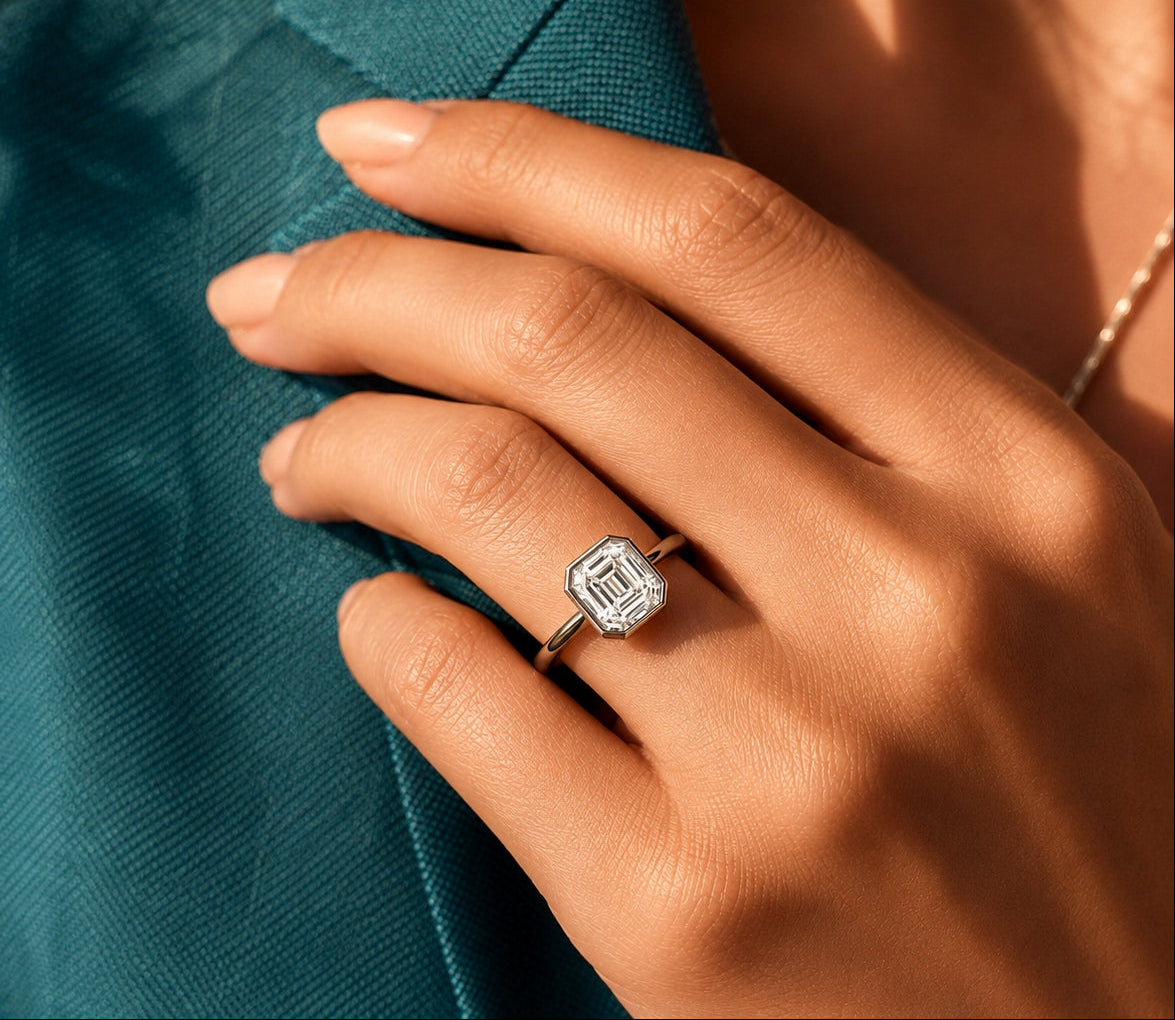 A close-up of a hand wearing a white gold ring with an asscher cut clear daimond, resting on a teal blazer.